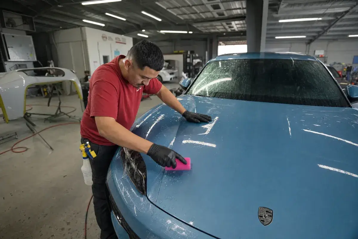 A technician squeegeeing paint protection film onto a hood at Podium Body Works in Round Rock, Texas