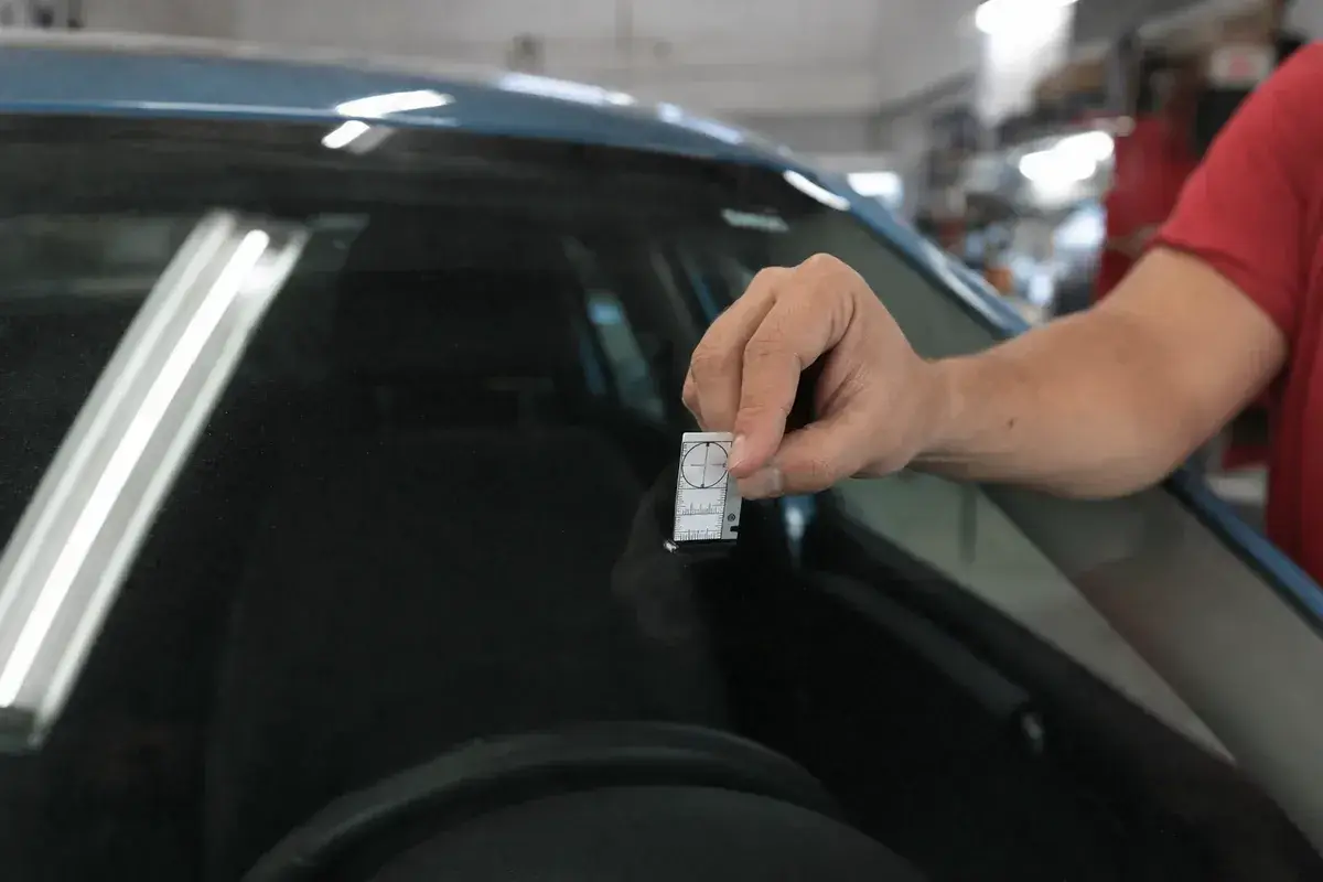 Gauging a windshield chip size before a resin repair at Podium Body Works in Round Rock, Texas