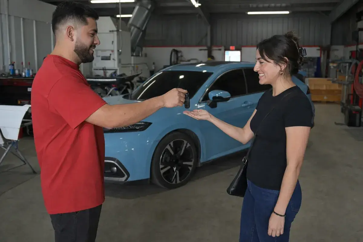 A happy customer receiving keys to their repaired car at Podium Body Works in Round Rock, Texas