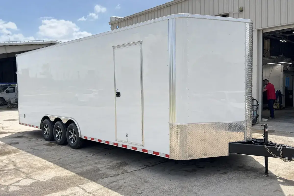 An enclosed vehicle transport trailer parked outside the shop at Podium Body Works in Liberty Hill, Texas