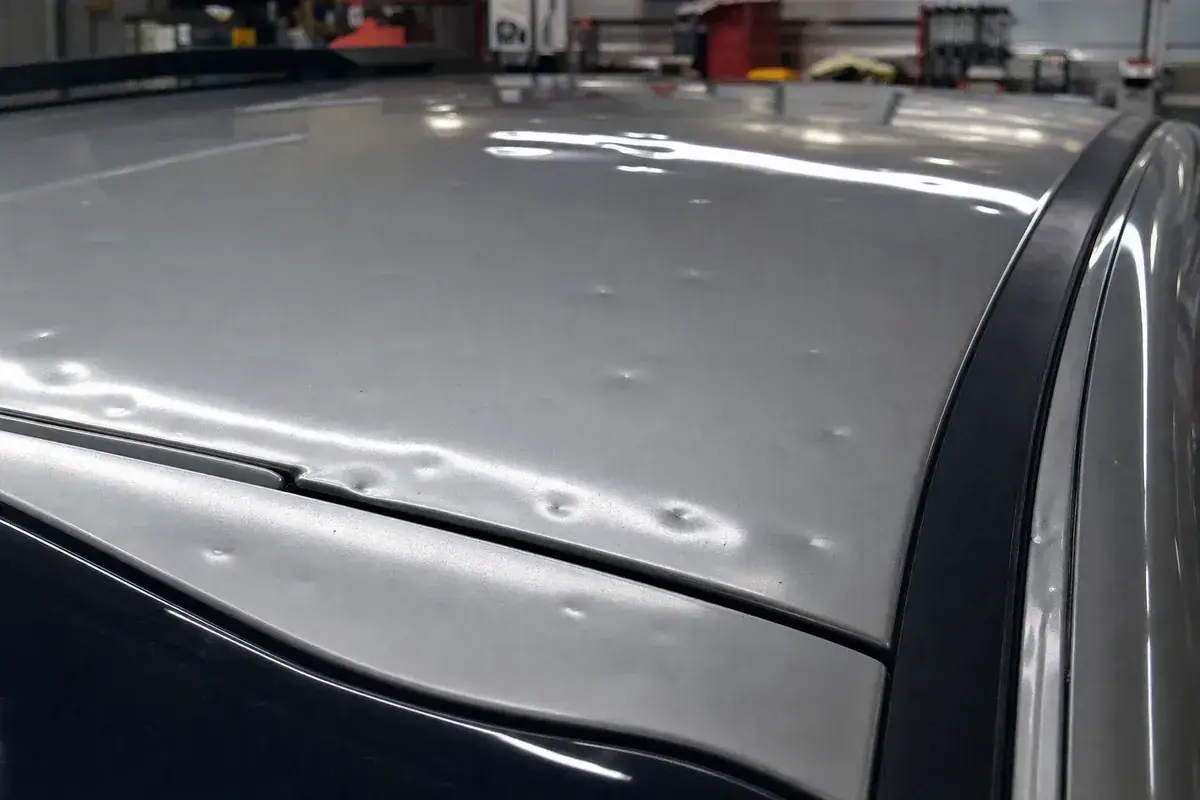 A car roof panel covered in small hail dents at Podium Body Works in Round Rock, Texas