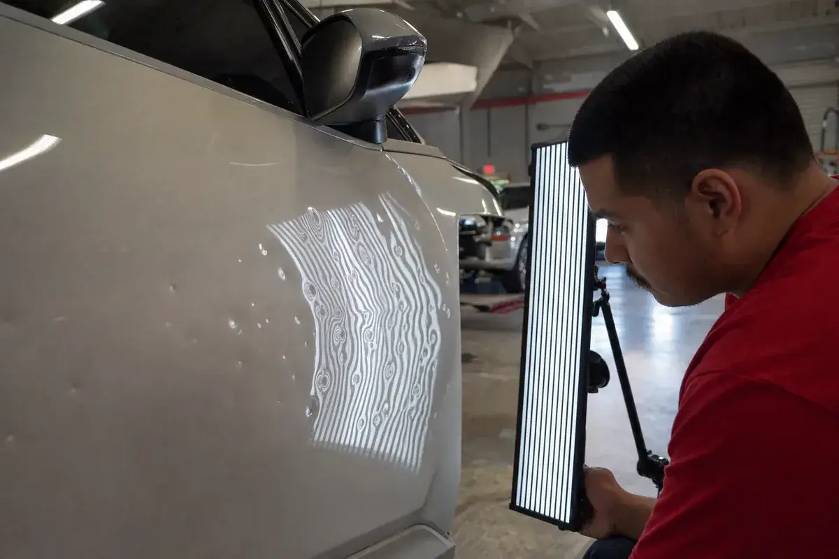 A hail-dented panel shown under a striped reflection board at Podium Body Works in Round Rock, Texas