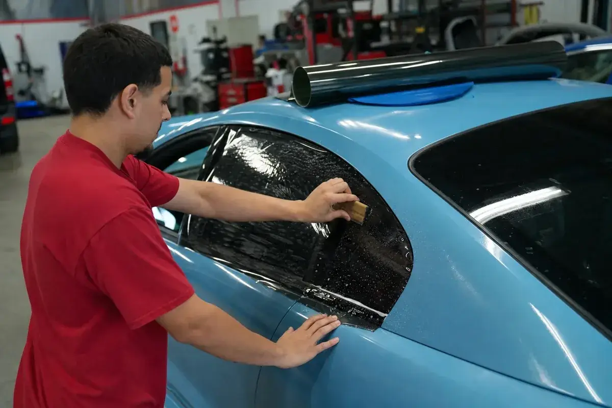 A technician installing ceramic window tint on a rear window at Podium Body Works in Round Rock, Texas