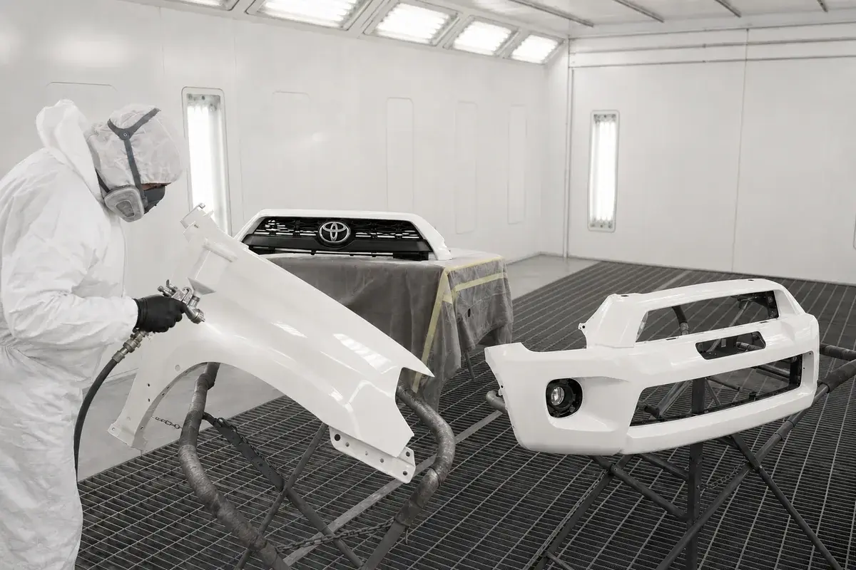 A painter spraying a white Toyota 4Runner fender and bumper in the paint booth at Podium Body Works in Round Rock, Texas