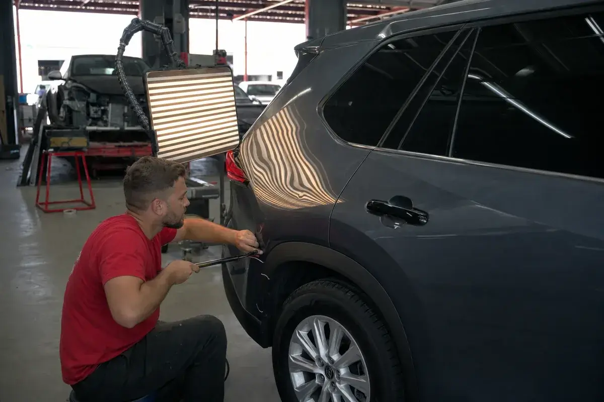 A reflection board over a panel showing a dent being worked at Podium Body Works in Round Rock, Texas