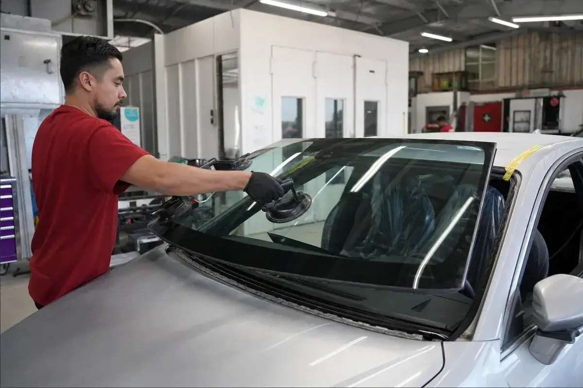 A technician setting a new windshield onto a sedan at Podium Body Works in Round Rock, Texas