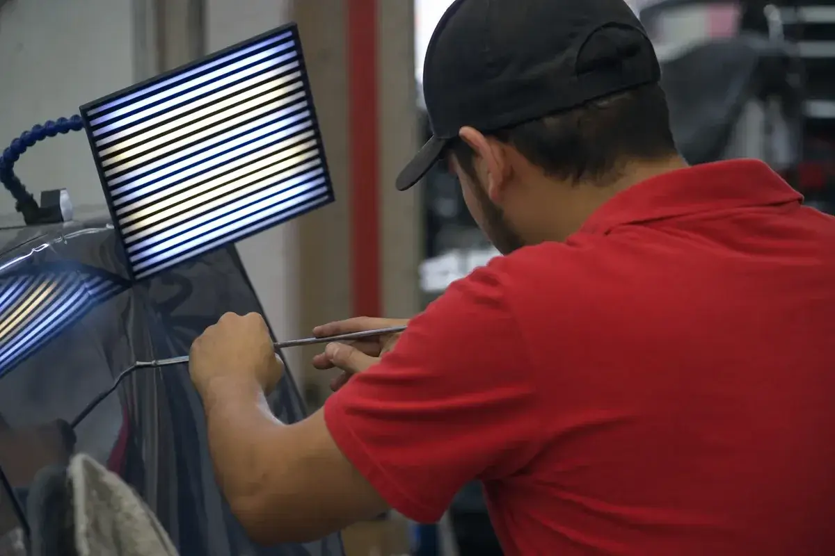 A technician working a dent with a paintless dent repair rod at Podium Body Works in Round Rock, Texas