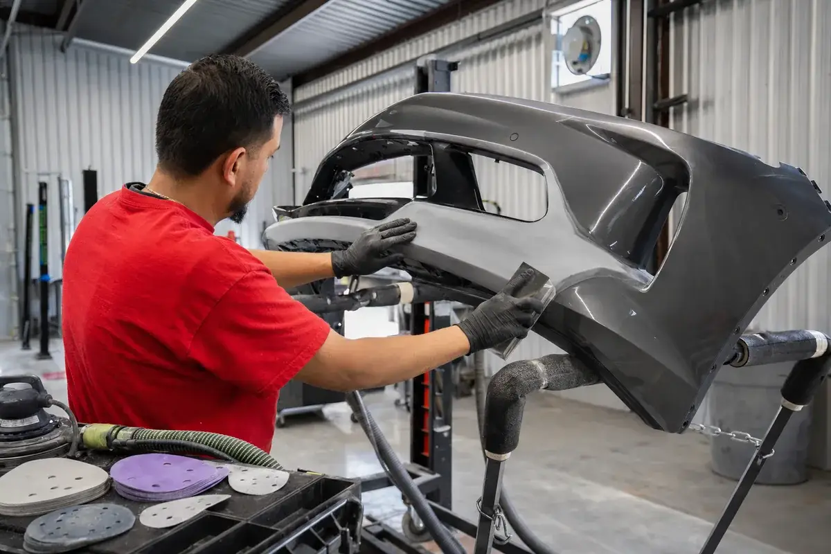 A technician sanding and prepping a silver bumper cover for refinishing at Podium Body Works