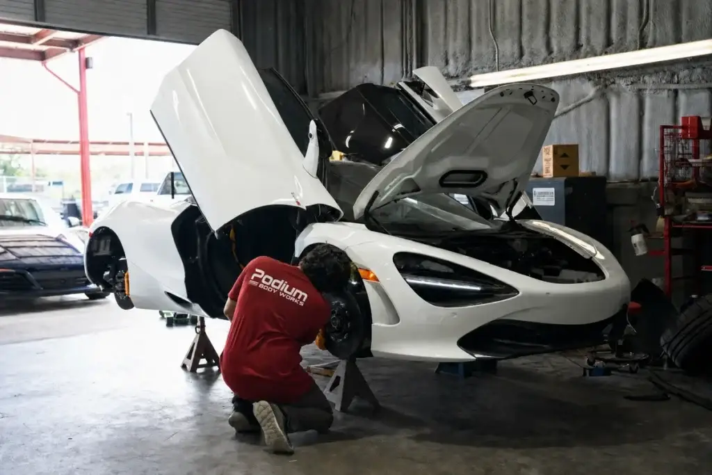 A technician in a red Podium Body Works shirt working on a white McLaren in the shop