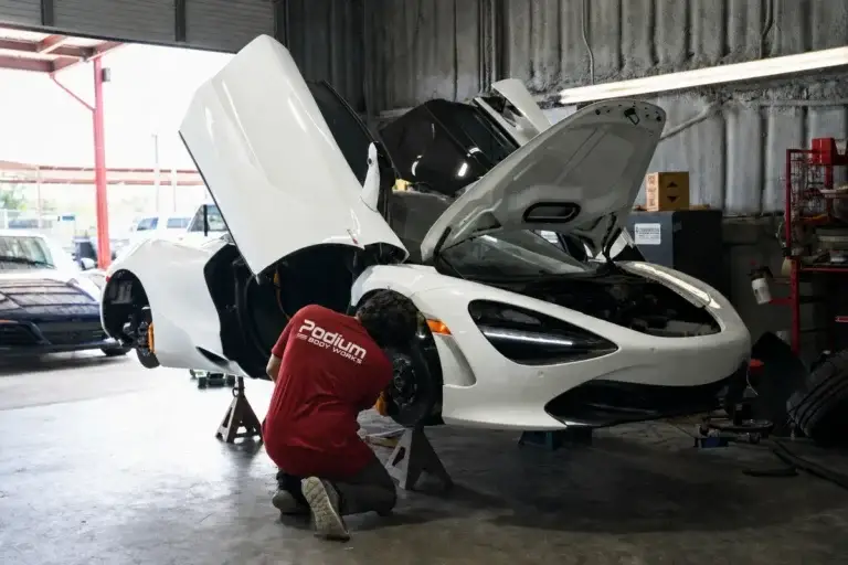 A technician in a red Podium Body Works shirt working on a white McLaren in the shop