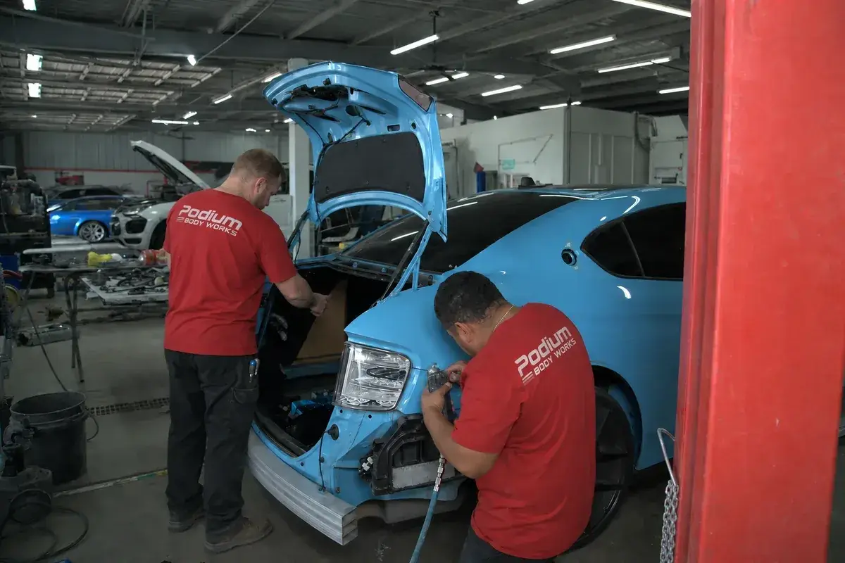 Two technicians working on a car in the shop at Podium Body Works in Round Rock, Texas