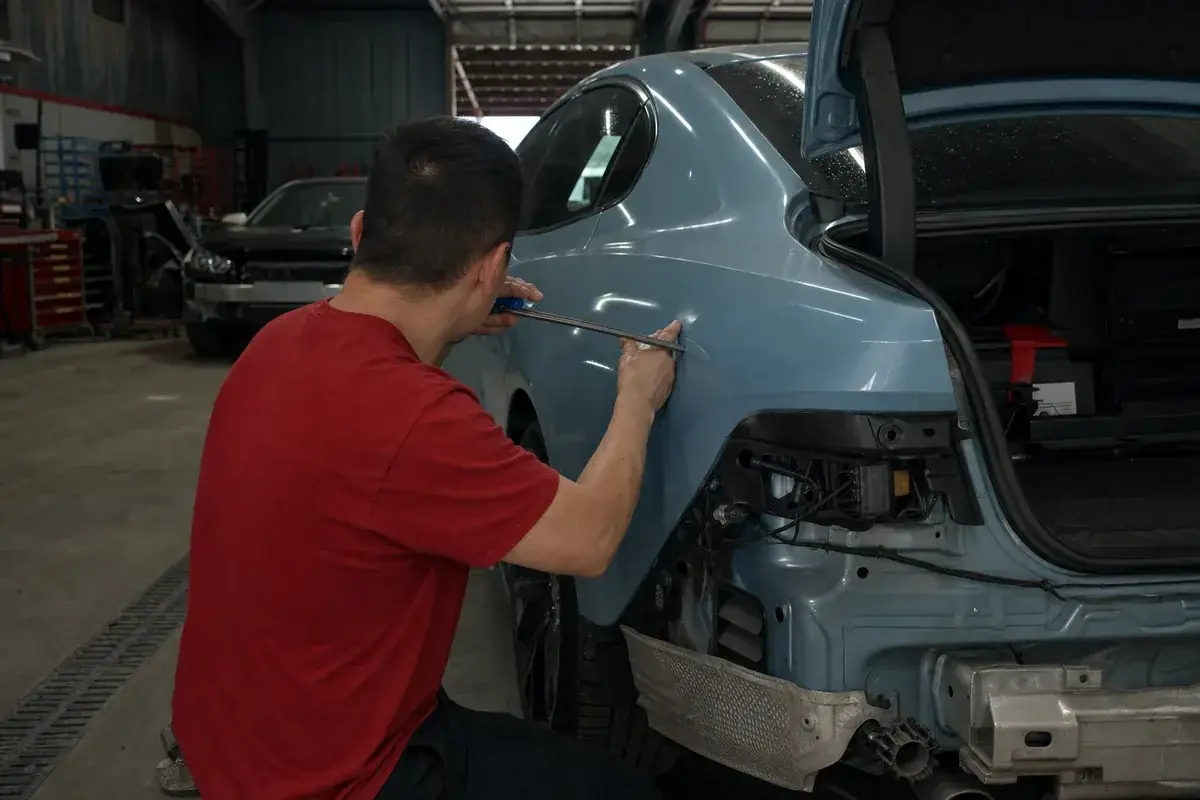 A technician working a dent from behind a panel with a rod at Podium Body Works in Round Rock, Texas
